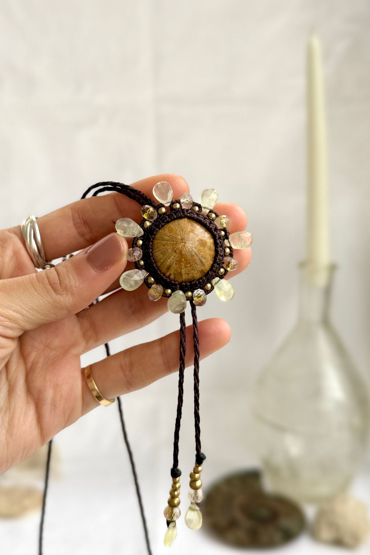 Sea urchin fossil bolo tie pendant held in hand, framed with prehnite and rutilated quartz beads, one of a kind statement jewelry