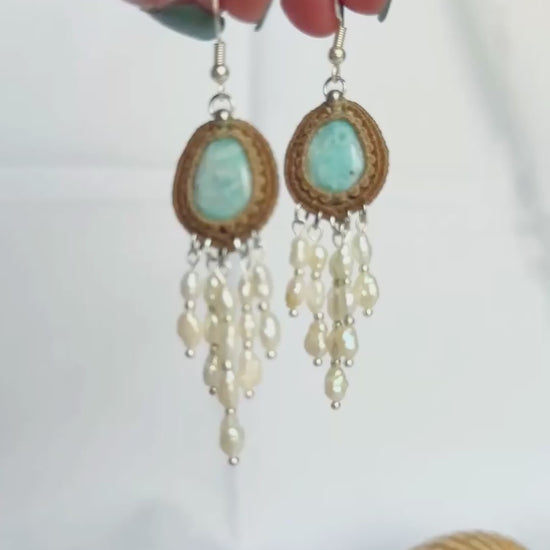 Hand holding Larimar macrame earrings showing the cascading freshwater pearls effect against a white background.