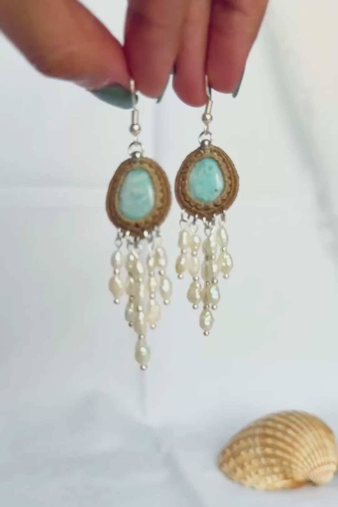 Hand holding Larimar macrame earrings showing the cascading freshwater pearls effect against a white background.