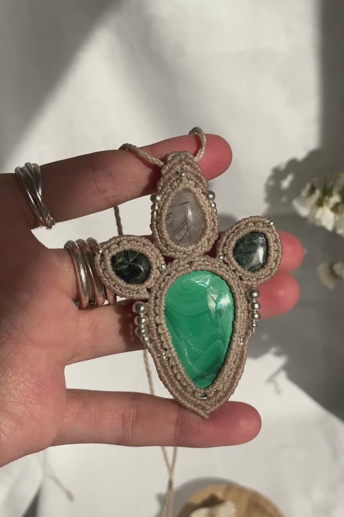 Close-up video of a handmade gemstone necklace, capturing the natural shine and intricate details of Malachite, Seraphinite and Tourmaline, Quartz. The unique design and polished gemstones reflect the light beautifully, highlighting the craftsmanship and one-of-a-kind artistry.