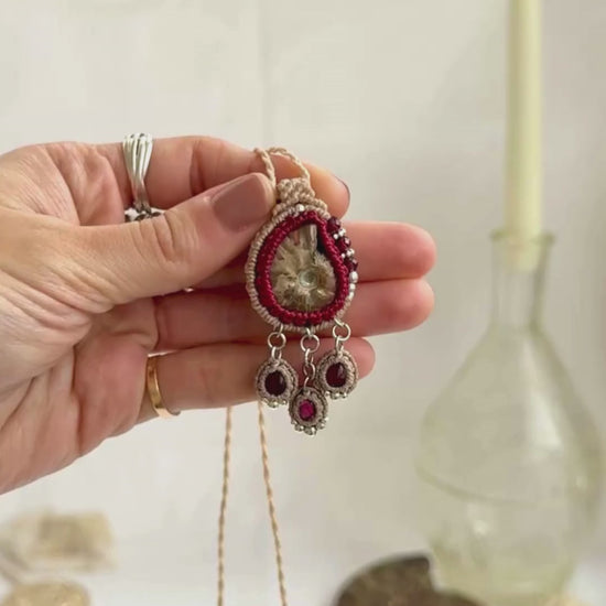 Ammonite fossil necklace with dangling garnet drops, highlighting iridescence and gemstone sparkle