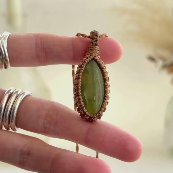Video showcasing the harmonious rare Vesuvianite gemstone showcasing a soft, subtle green hue, held in hand with its golden brown macrame necklace.