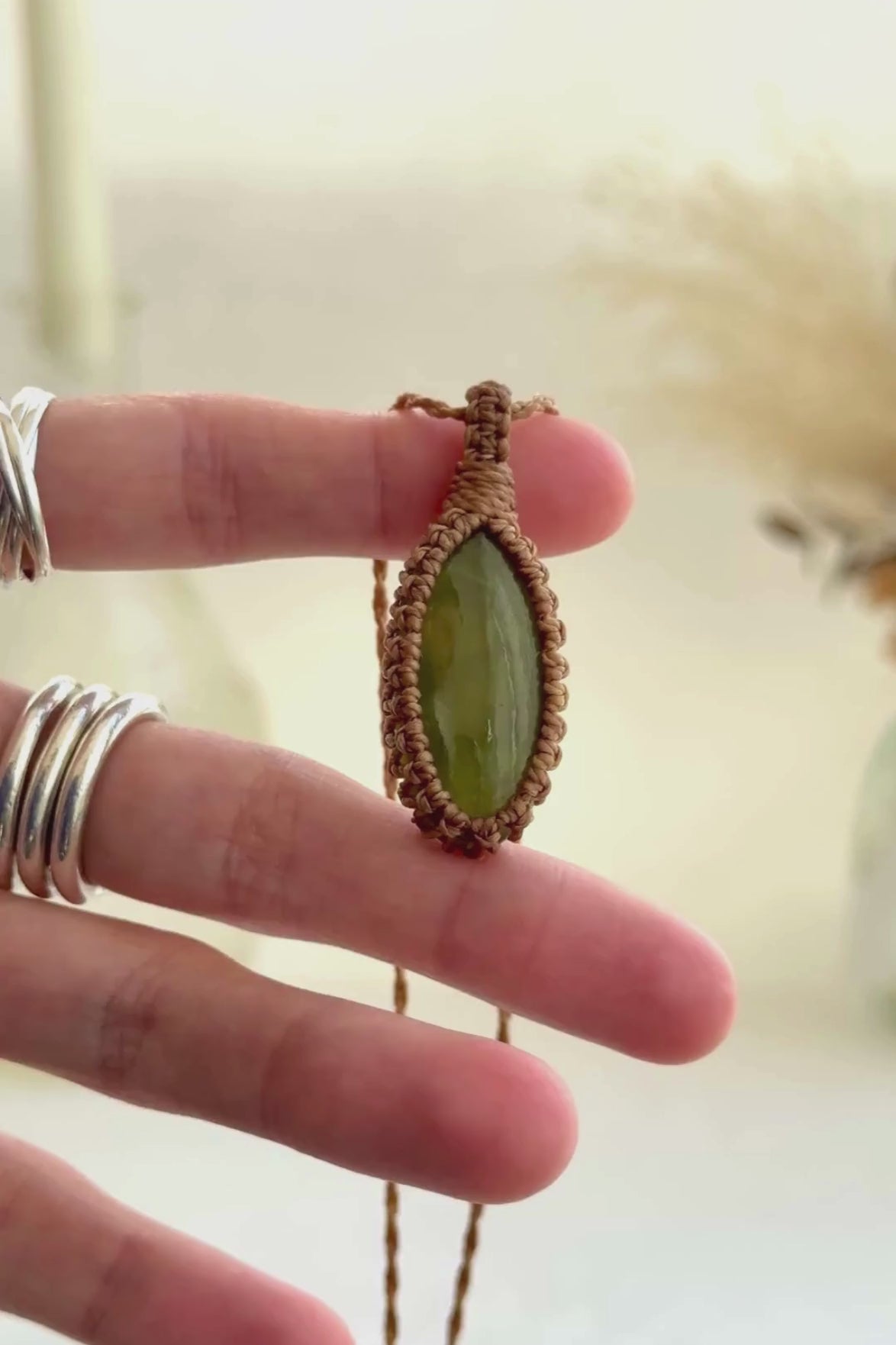 Video showcasing the harmonious rare Vesuvianite gemstone showcasing a soft, subtle green hue, held in hand with its golden brown macrame necklace.