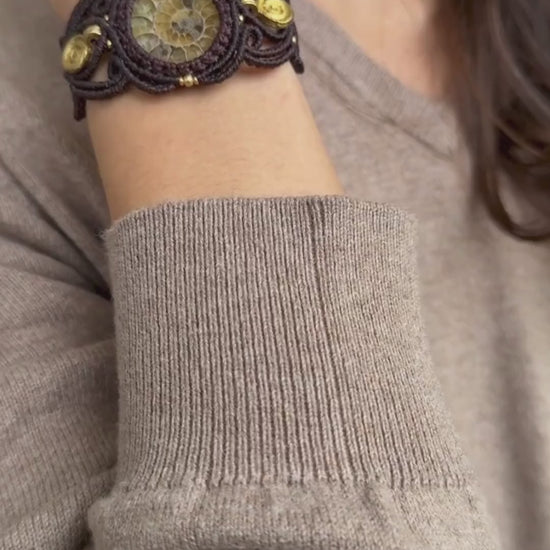 Yellow ammonite cuff bracelet in motion on wrist, showing spiral brass accents, fossil detail, and adjustable fit