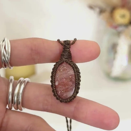 Video showcasing the harmonious vibrant Sunstone gemstone that holds a mysterious beauty, revealing a subtle shimmer when touched by light, held in hand with its dark green macrame necklace.
