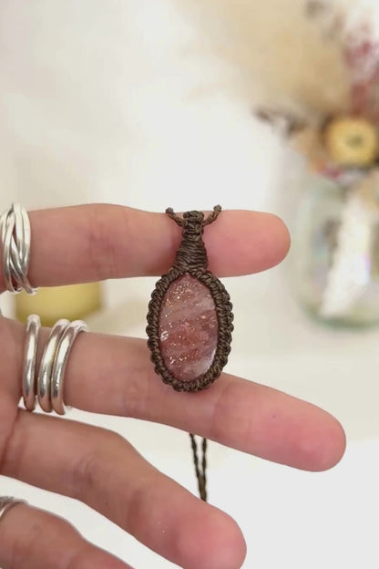 Video showcasing the harmonious vibrant Sunstone gemstone that holds a mysterious beauty, revealing a subtle shimmer when touched by light, held in hand with its dark green macrame necklace.