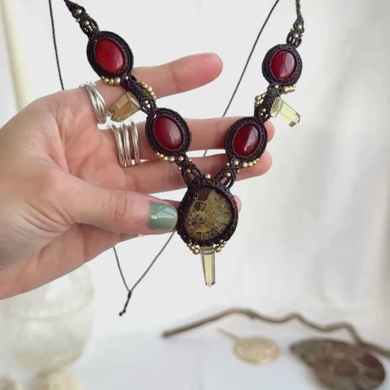 Video showing V-shaped ammonite necklace with central yellow ammonite, carnelian stones, smoky quartz points, and macramé craftsmanship, highlighting stone shine and detail