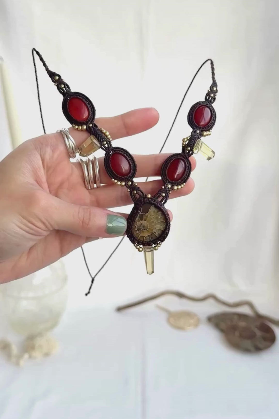 Video showing V-shaped ammonite necklace with central yellow ammonite, carnelian stones, smoky quartz points, and macramé craftsmanship, highlighting stone shine and detail
