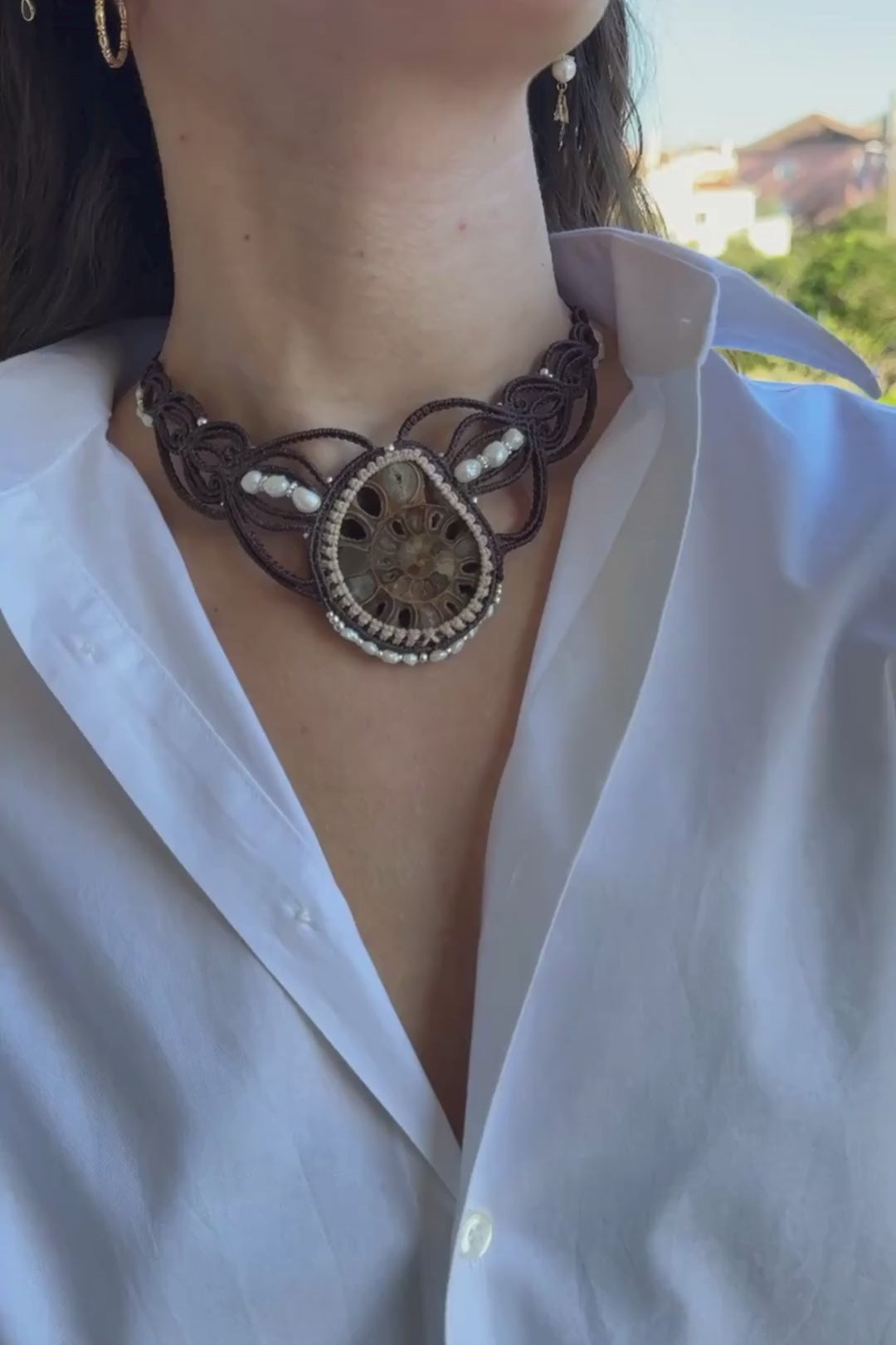 Video showing model wearing large ammonite fossil statement necklace with freshwater pearls, close-up of crystal-lined ammonite and macramé details